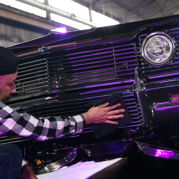 Detailing a Chevrolet: Man wipes down the grill of a classic black car with a cloth, lit with purple neon.
